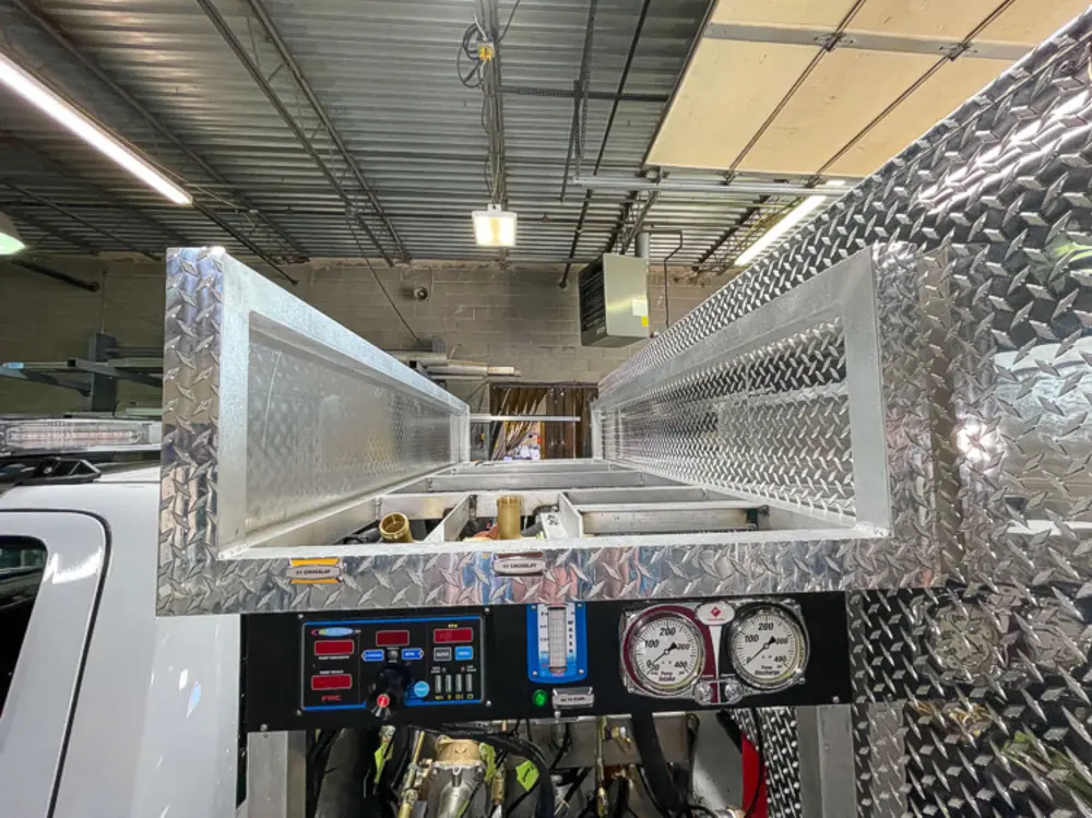 Exterior view of small fire truck showing cab, body compartments, and wheel/tire area.